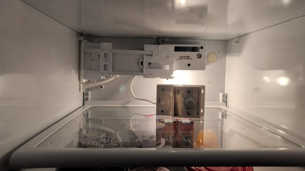 Refrigerator ice maker assembly exposed inside the upper compartment.
