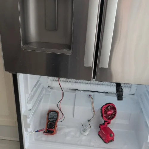 Stainless refrigerator open with diagnostic tools inside during repair.
